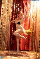 A woman in a bikini is dancing in front of a curtain.