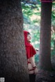 A woman in a red hooded outfit standing next to a tree.