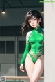 A woman in a green and white leotard leaning against a wall.